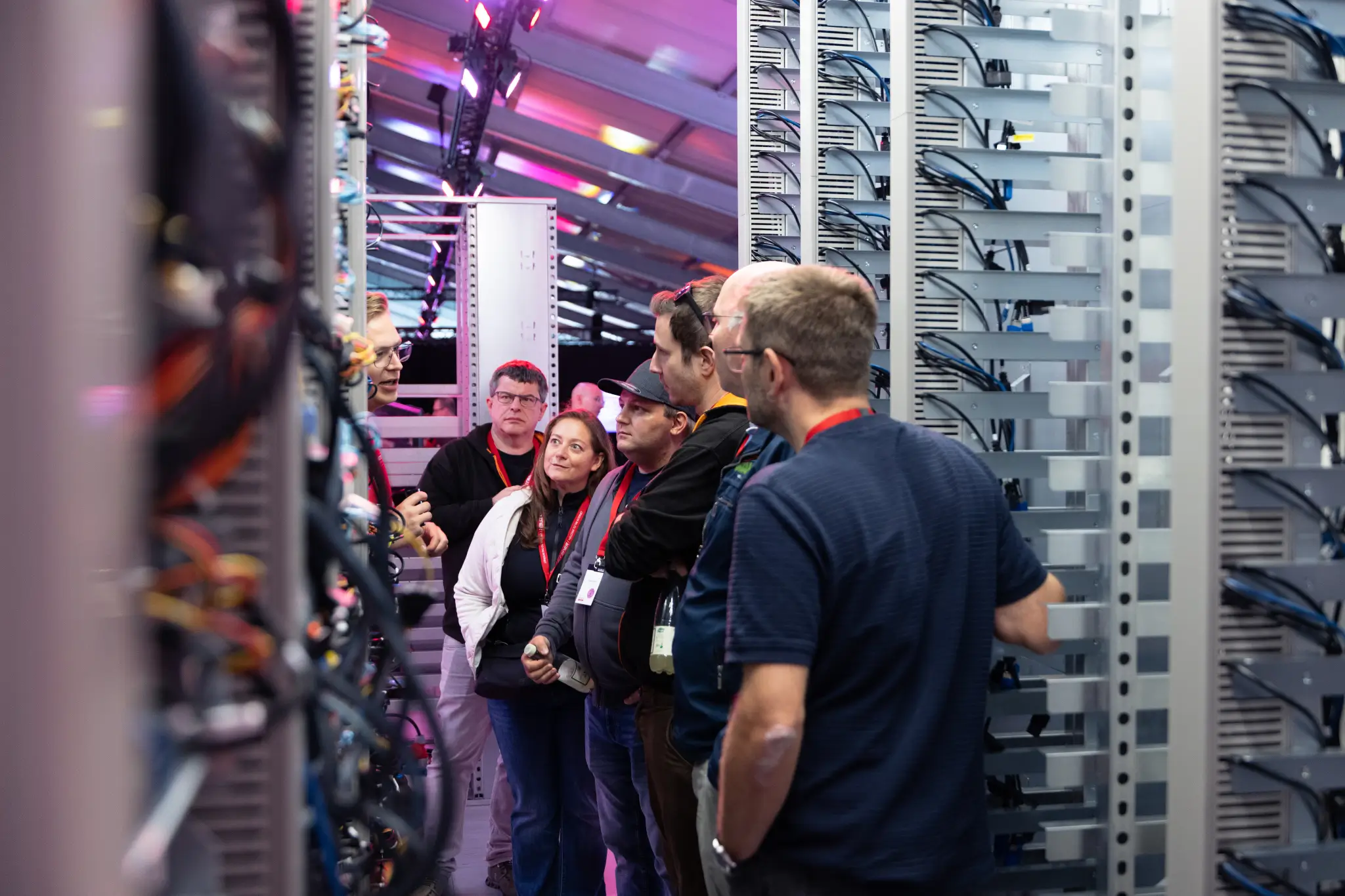 Visitors wearing headsets stand in an aisle between server racks, listening.