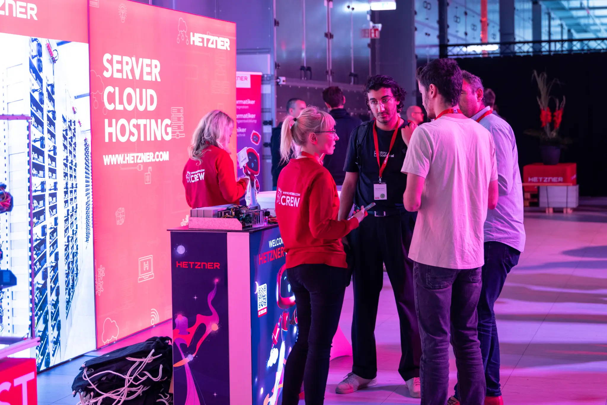 Booth with a red "Server Cloud Hosting" banner, guests and Hetzner people operations team talking in front.