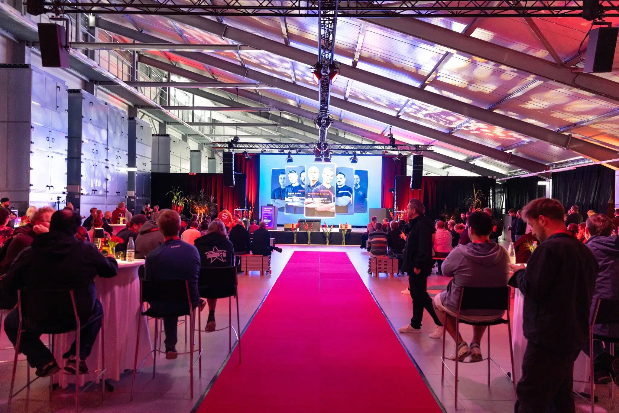 Data center with a red carpet leading to the stage, guests seated waiting for the next session to start.