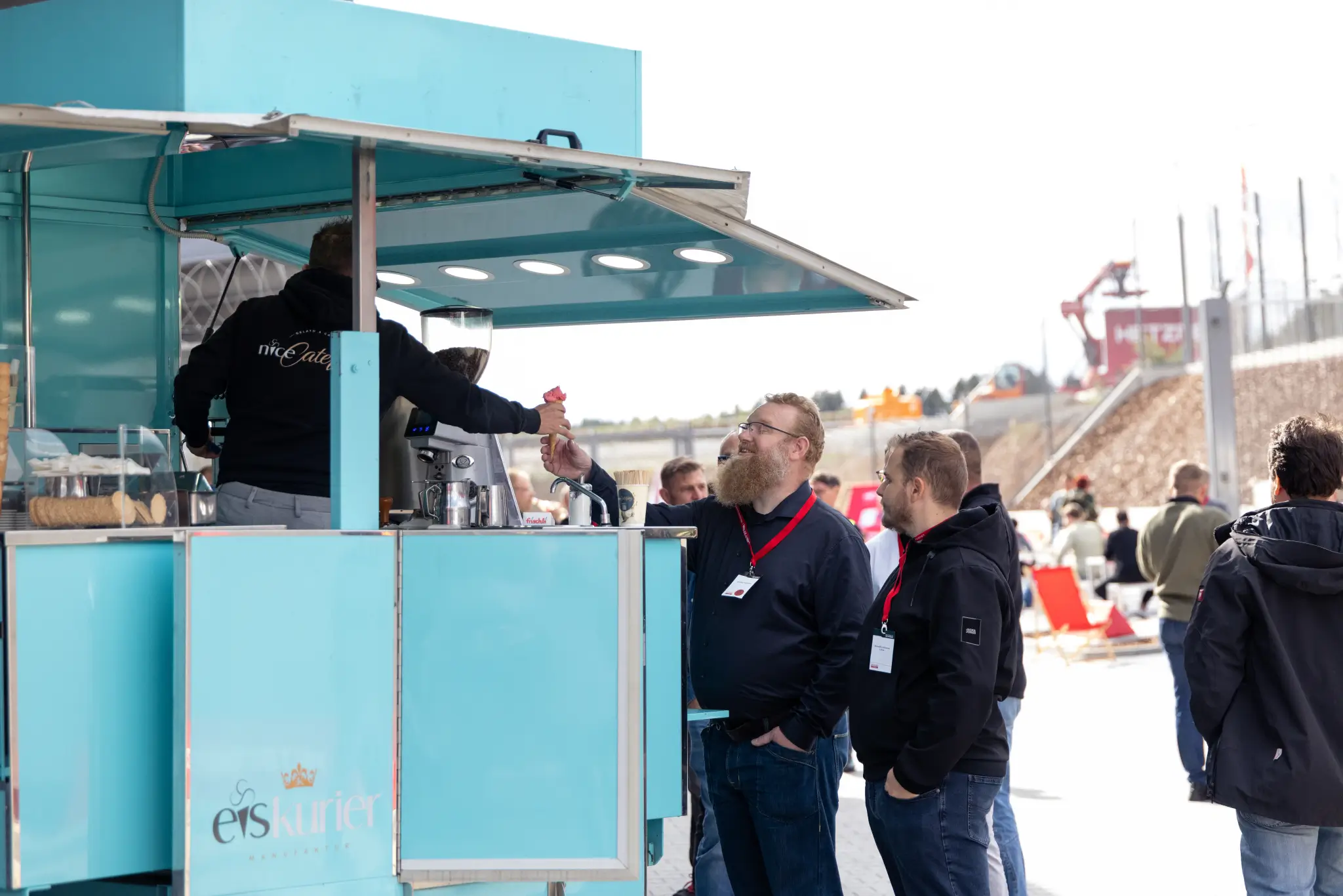 Turquoise serving stand outdoors with guests wearing Hetzner lanyards standing in front.