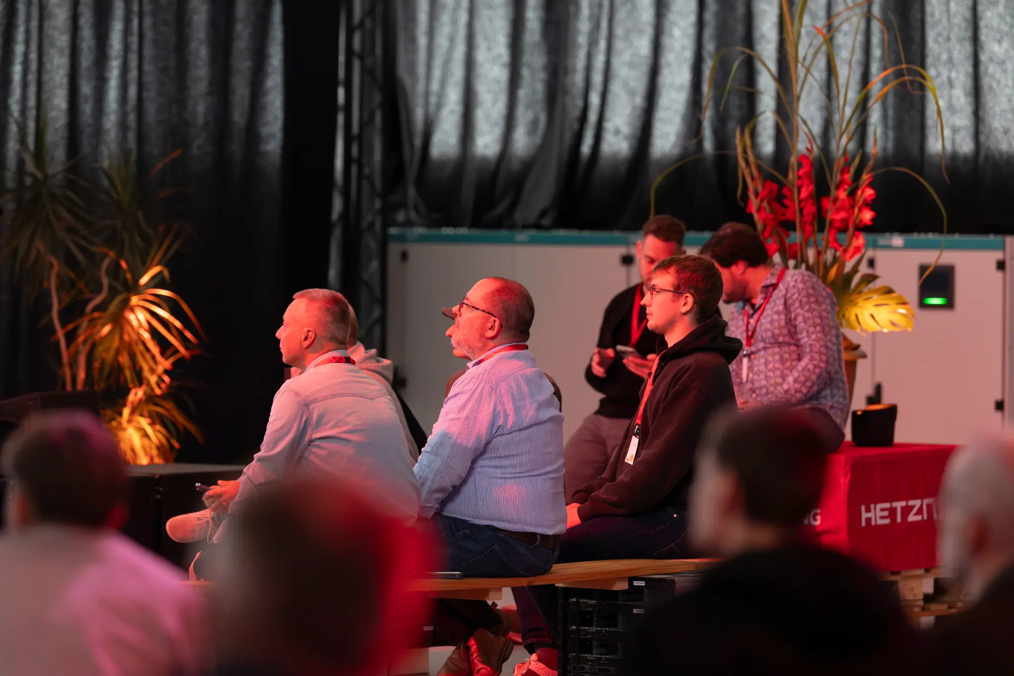 Guests seated in a in front of dark curtains and flower arrangements listening to Hetzner Sessions.