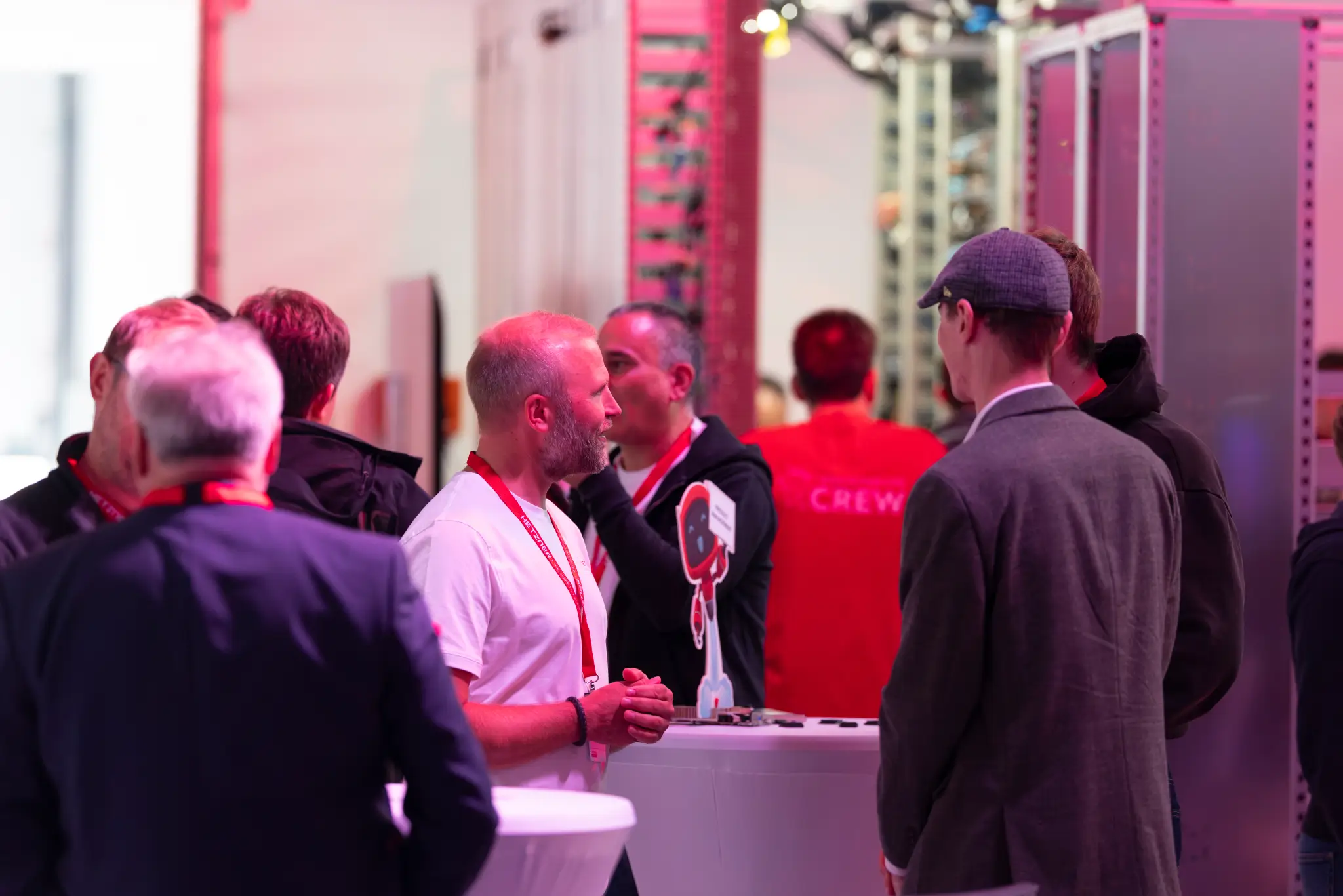 Guests stand talking to Hetzner employees in front of server racks at the Hetzner Summit. 